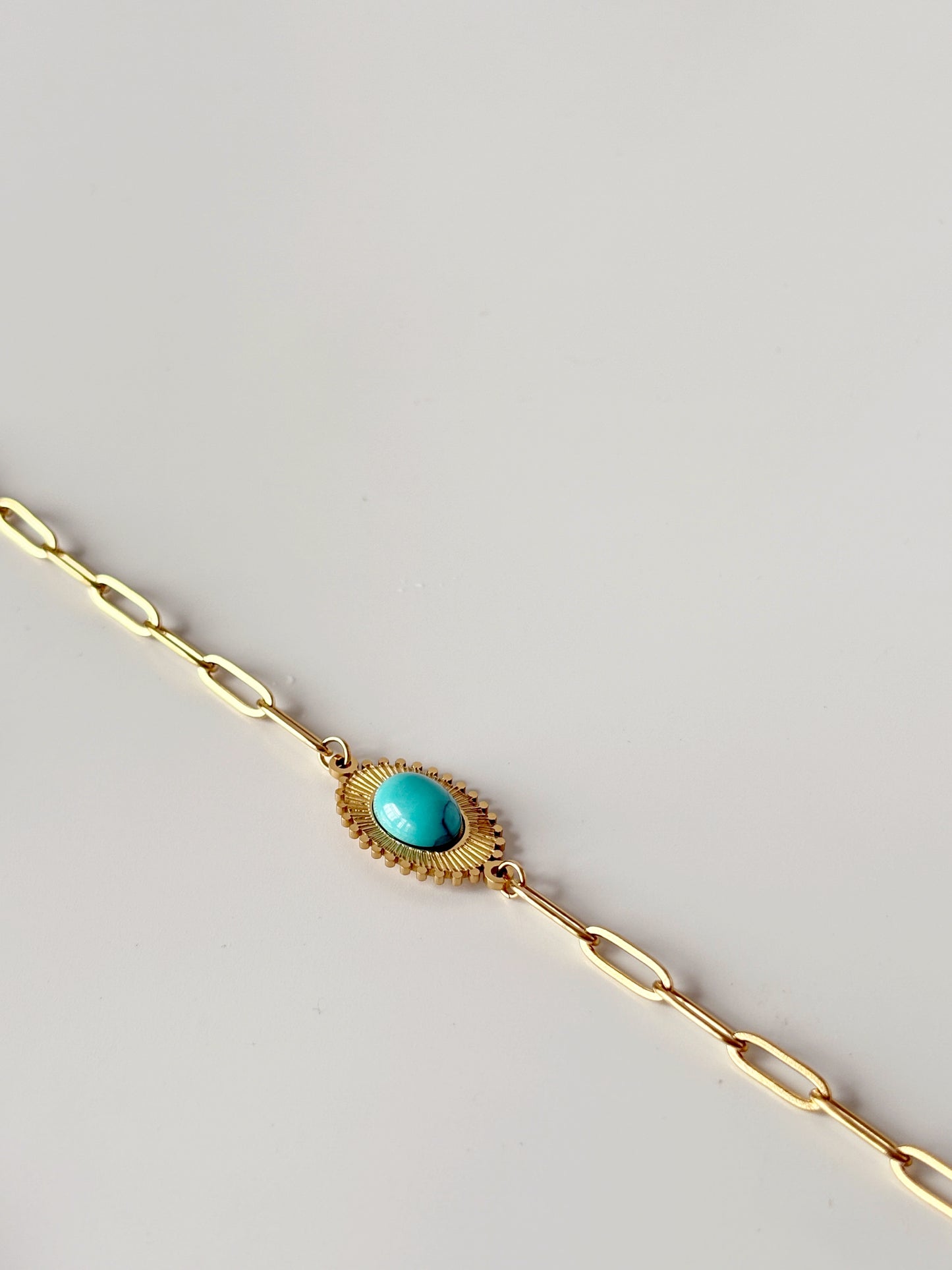Gold bracelet with a turquoise stone on a light gray background