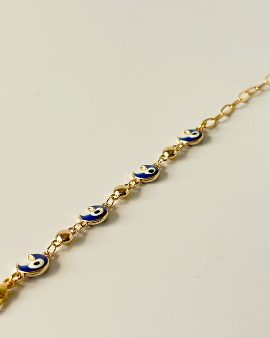 Gold bracelet with blue evil eye charms on a light gray background