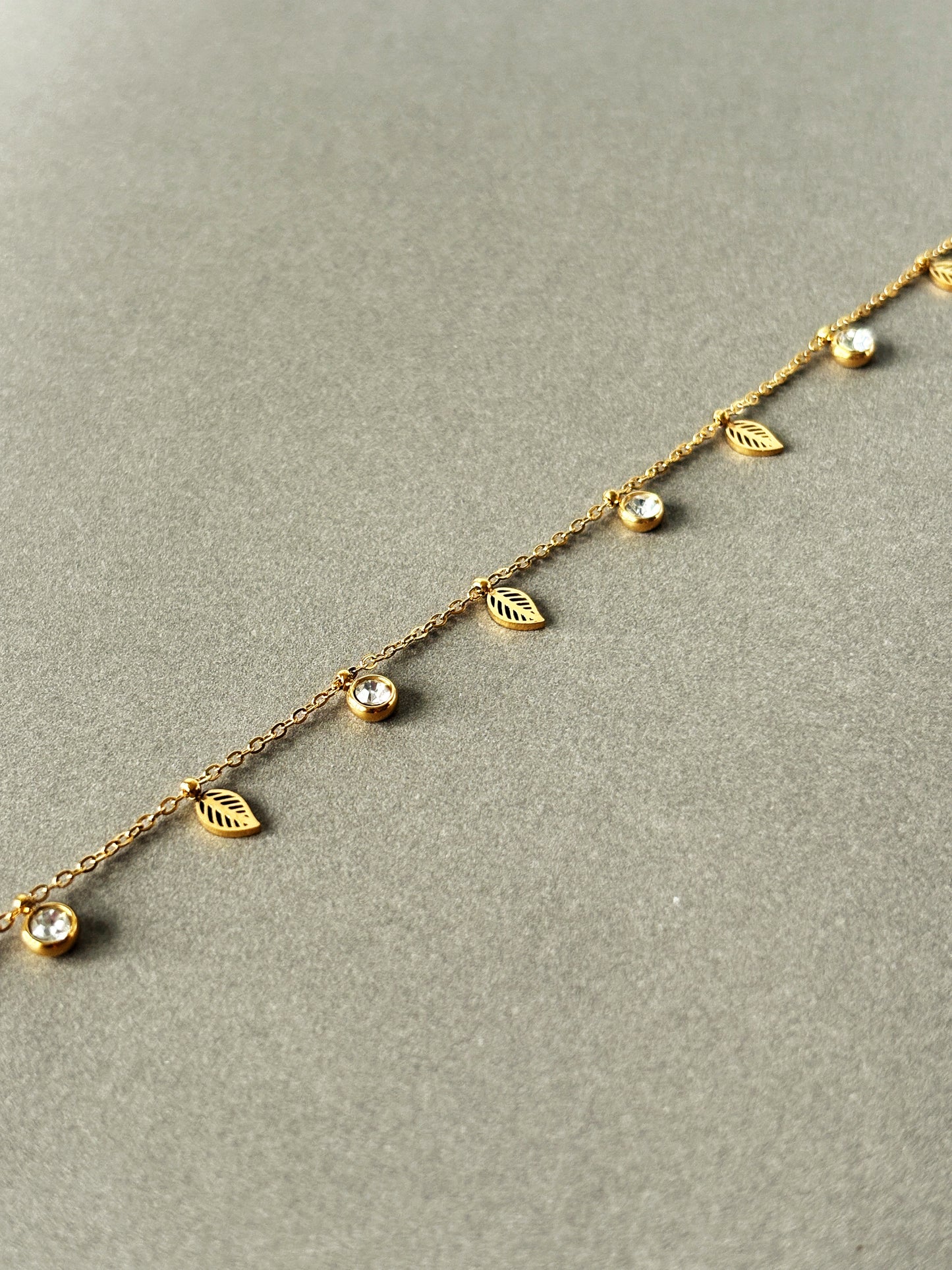 Gold bracelet with leaf and gemstone details on a gray background