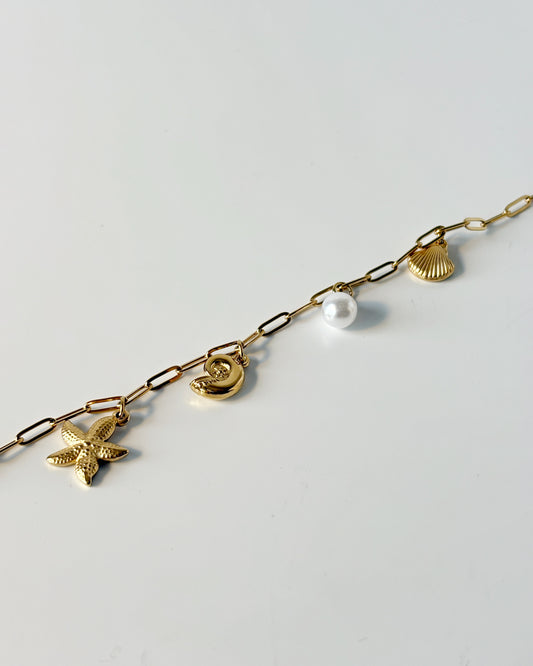 Gold chain bracelet with various charms on a light gray background