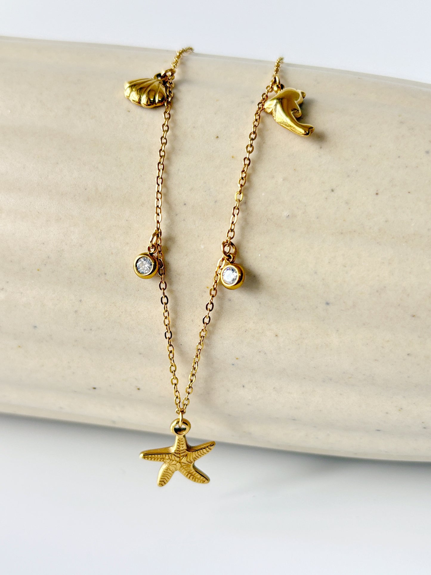Gold necklace with starfish and shell pendants on a beige surface