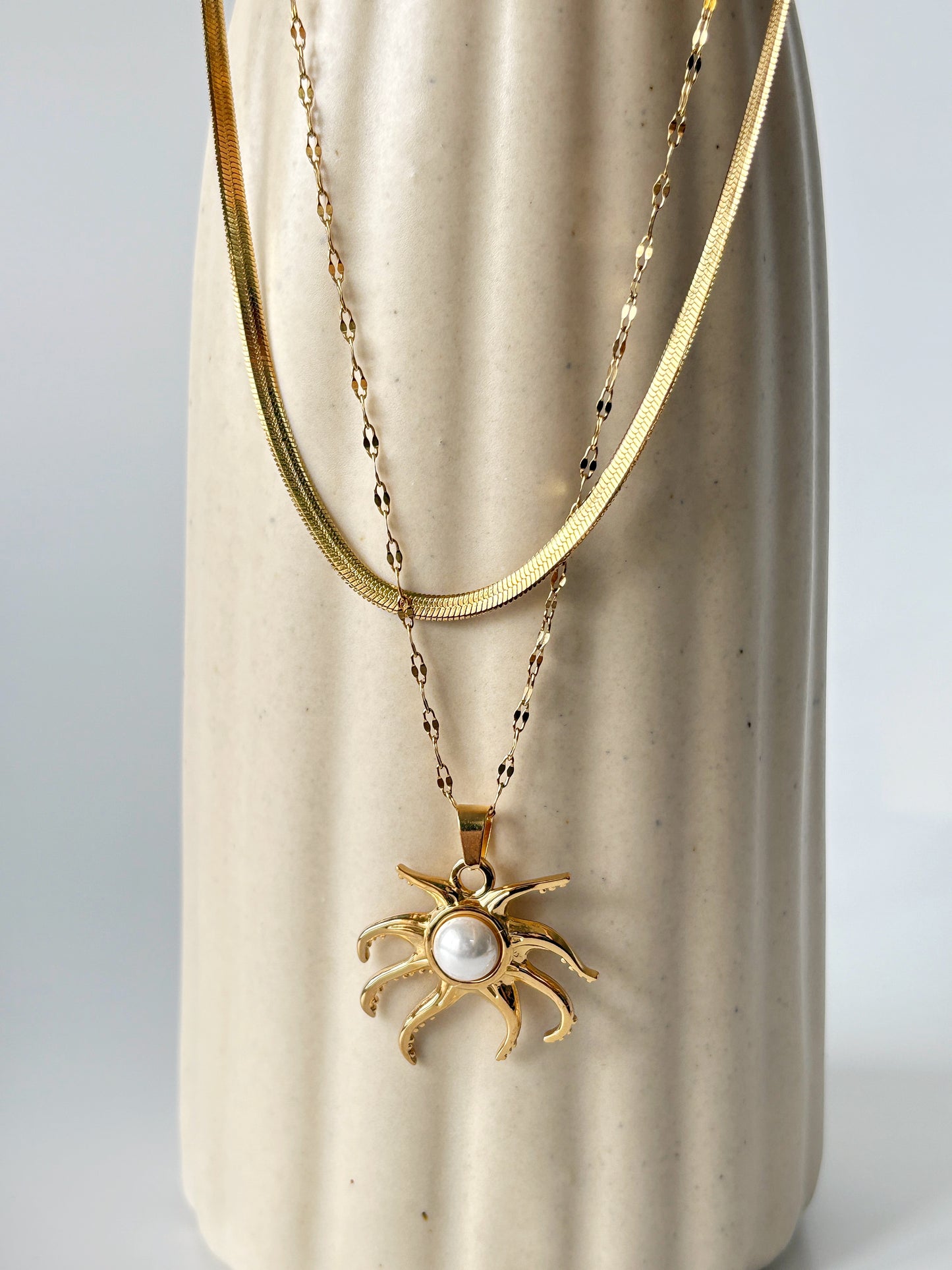Gold necklace with a sun-shaped pendant on a beige ceramic vase.