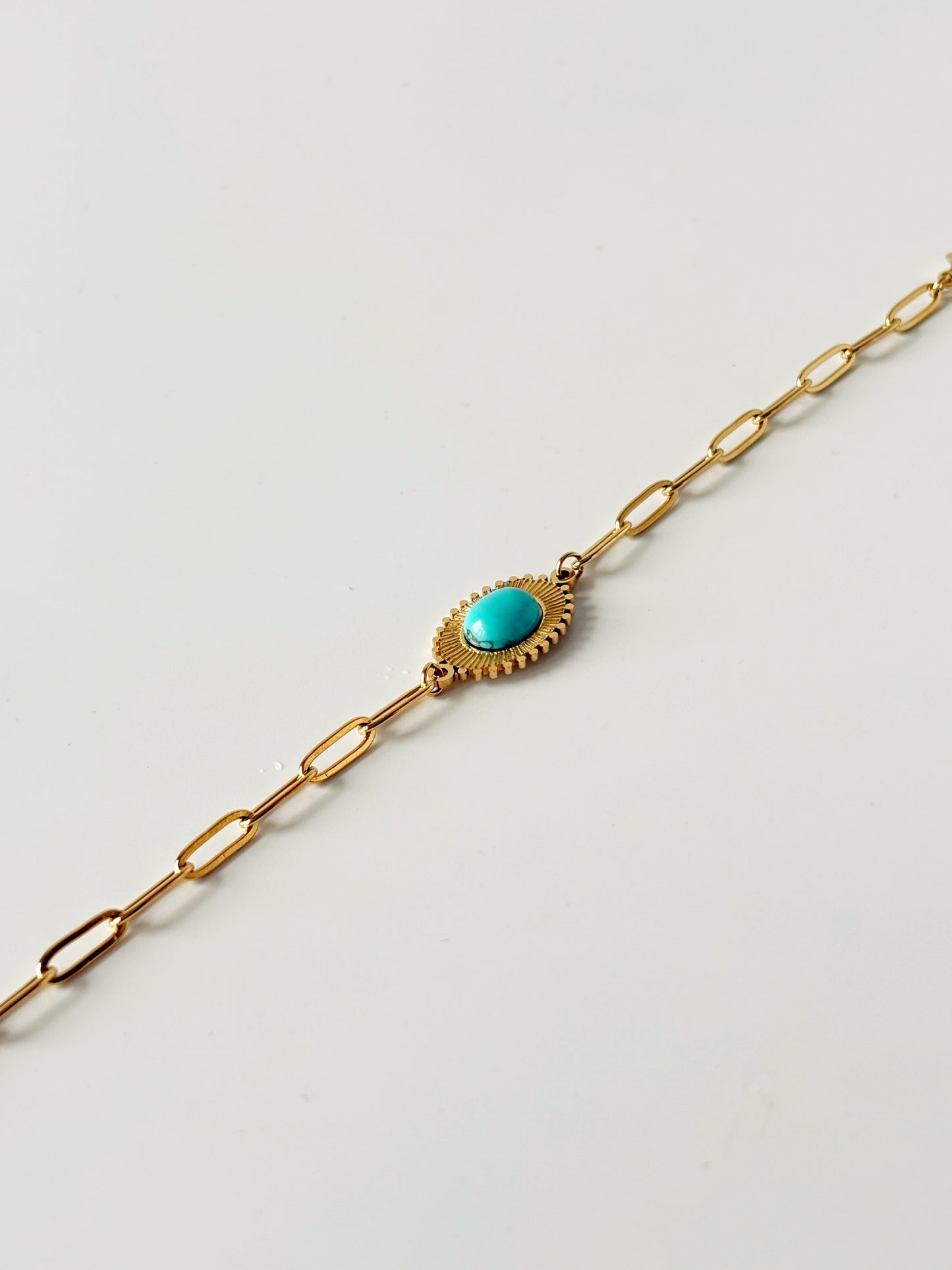 Gold bracelet with a turquoise stone on a light gray background
