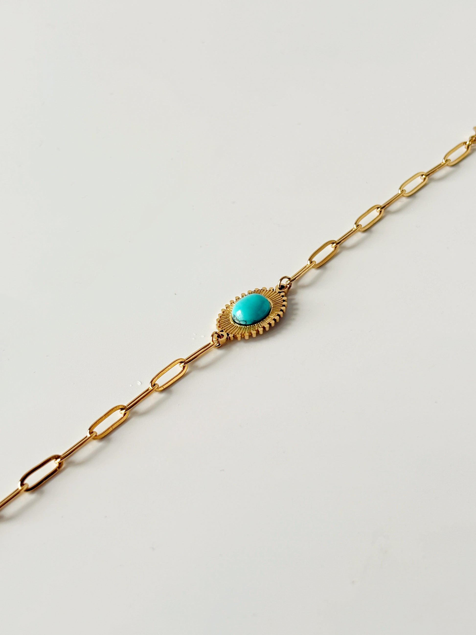 Gold bracelet with a turquoise stone on a light gray background