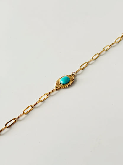 Gold bracelet with a turquoise stone on a light gray background