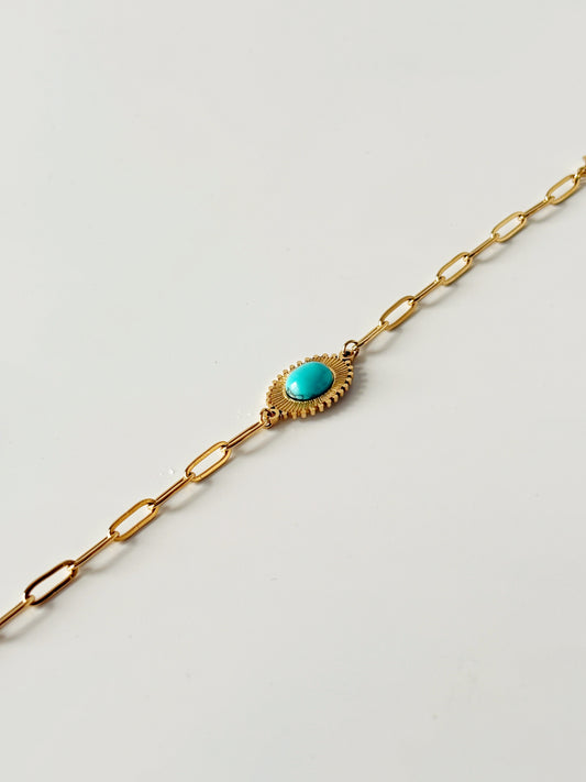 Gold bracelet with a turquoise stone on a light gray background
