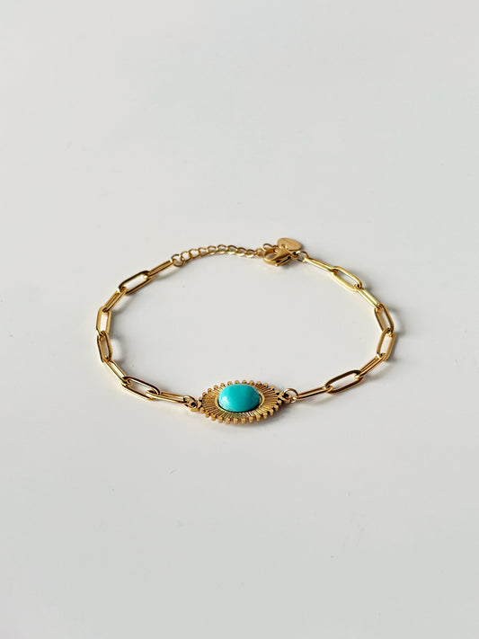 Gold bracelet with a turquoise stone on a light gray background