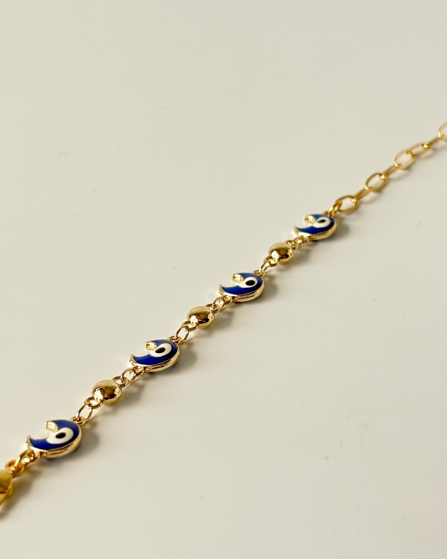 Gold bracelet with blue evil eye charms on a light gray background