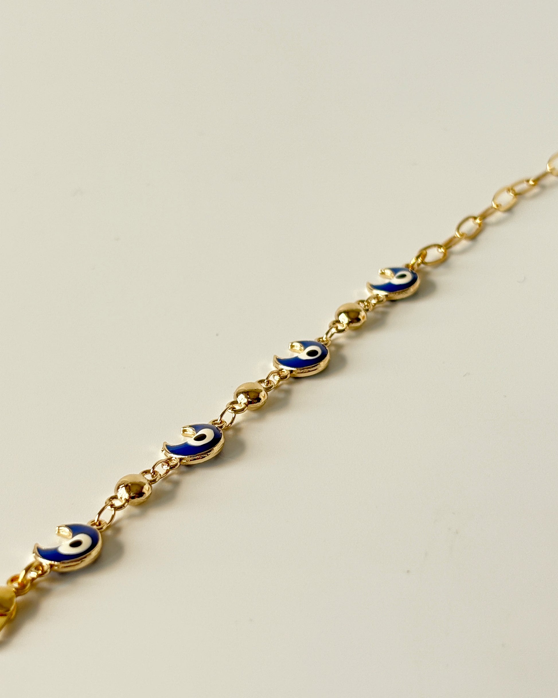 Gold bracelet with blue evil eye charms on a light gray background