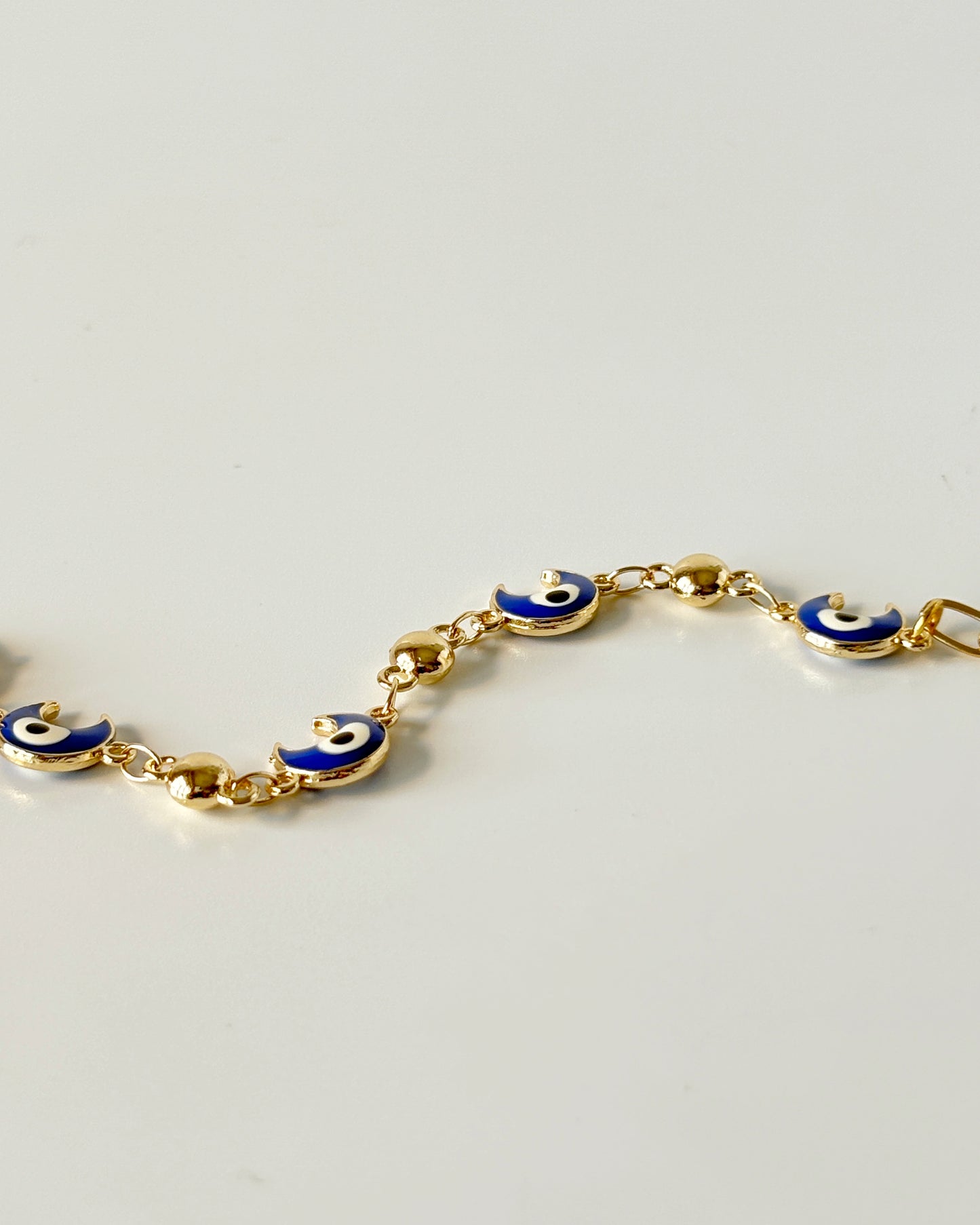 Gold bracelet with blue evil eye charms on a light gray background
