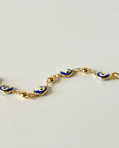 Gold bracelet with blue evil eye charms on a light gray background