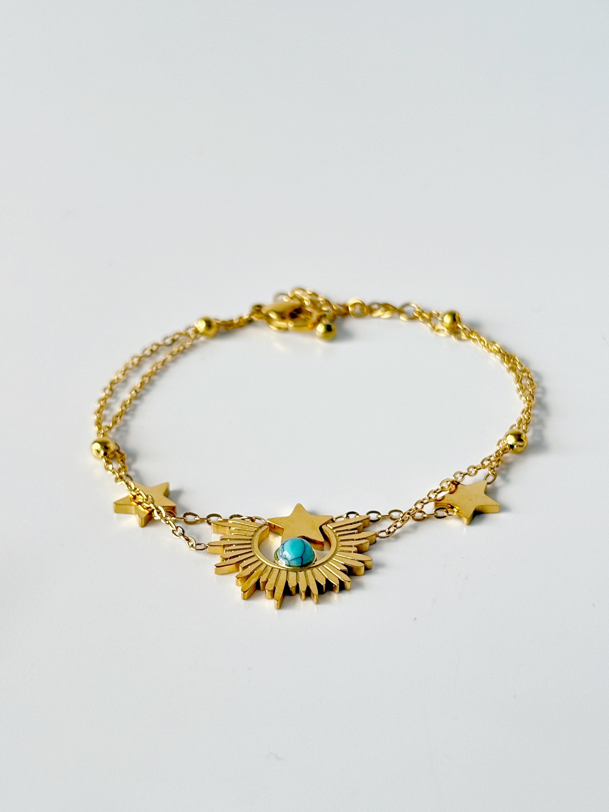 Gold bracelet with star and sun designs on a light gray background