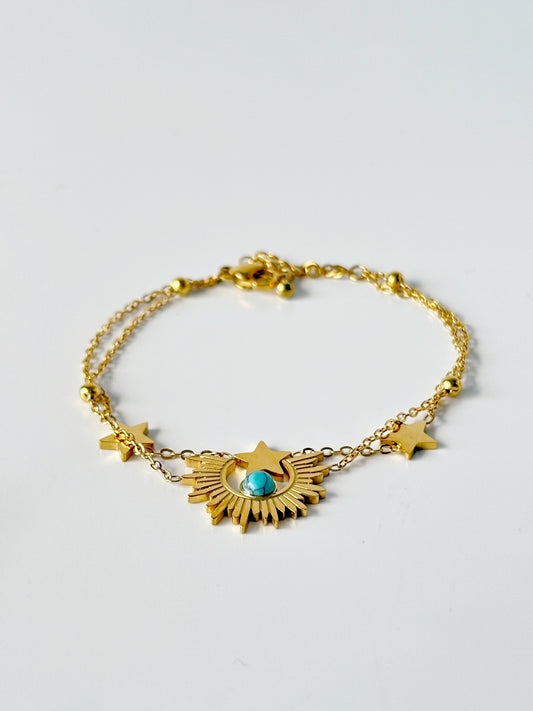 Gold bracelet with star and sun designs on a light gray background