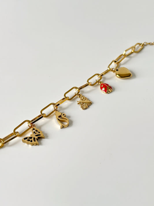 Gold chain bracelet with various charms on a light gray background