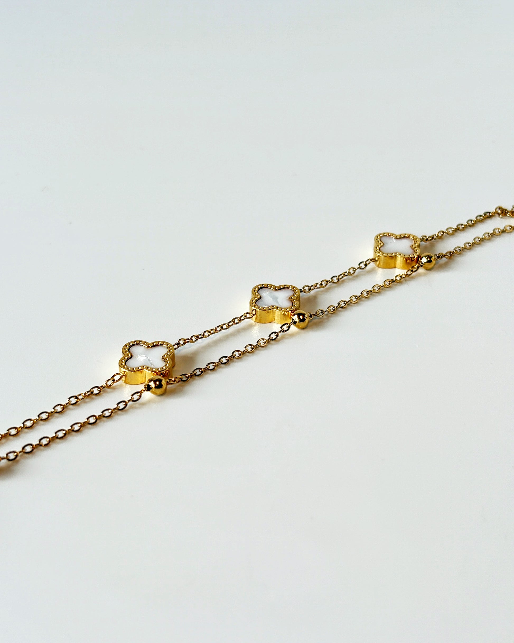 Gold chain clover necklace on a light gray background