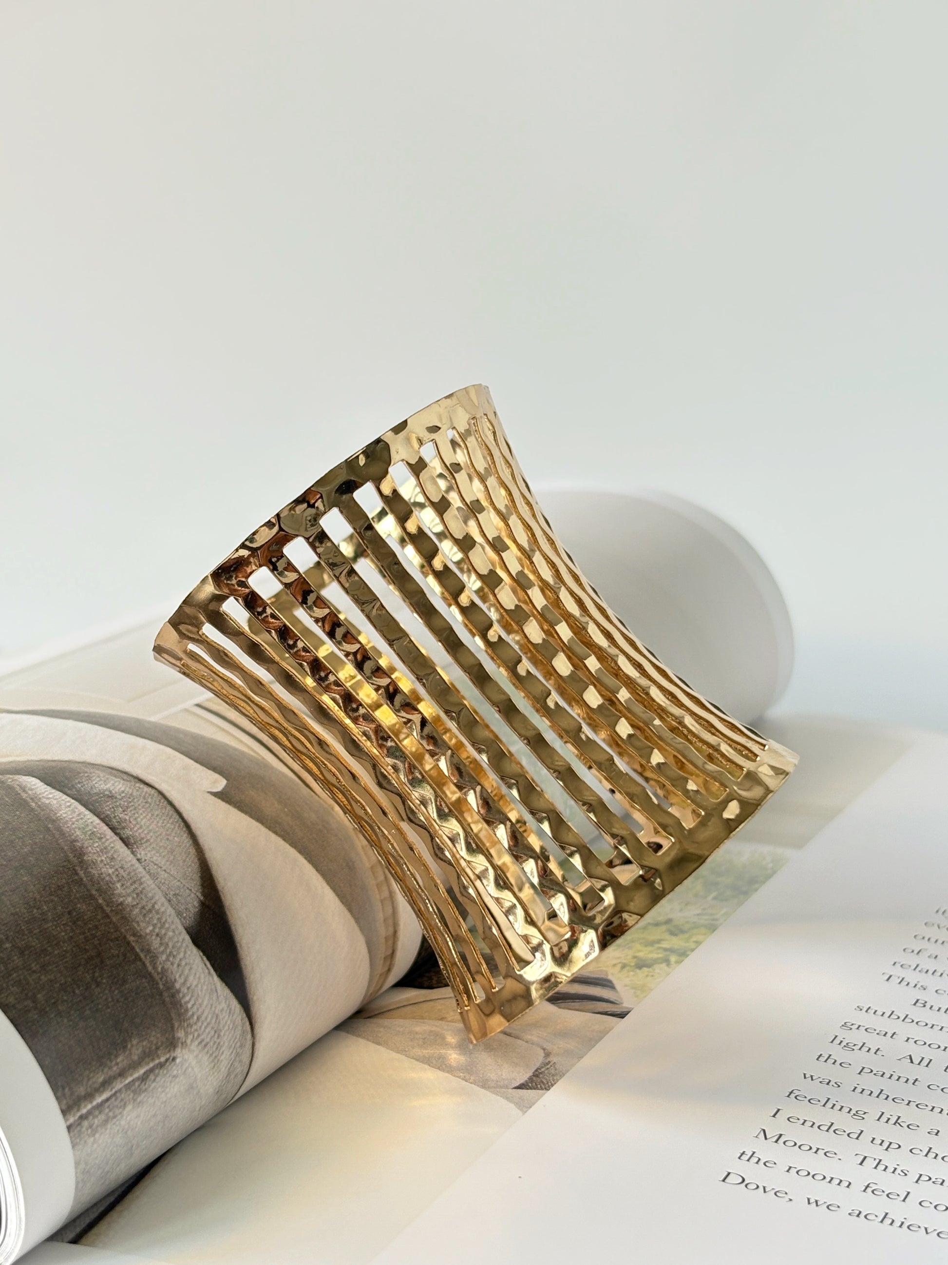 Gold bracelet cuff on an open book with a white background