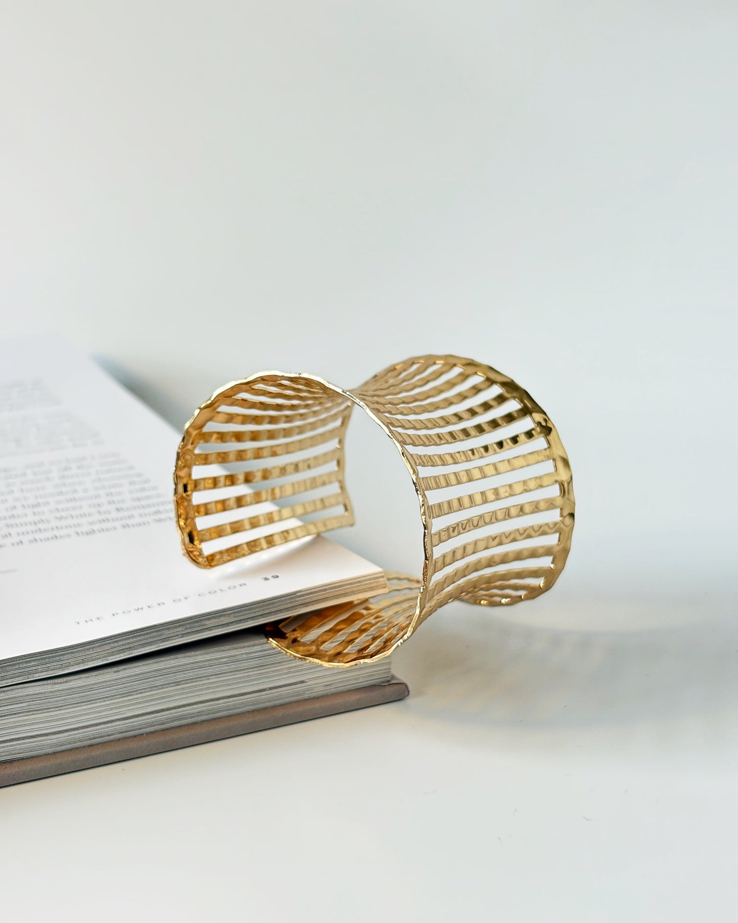 Gold bracelet cuff on an open book with a white background