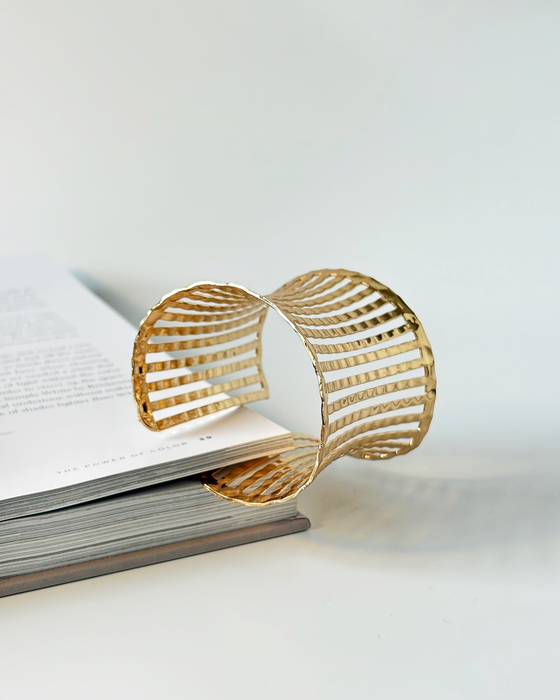 Gold bracelet cuff on an open book with a white background