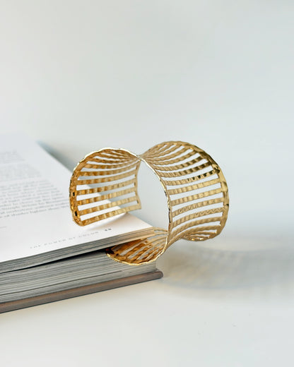 Gold bracelet cuff on an open book with a white background