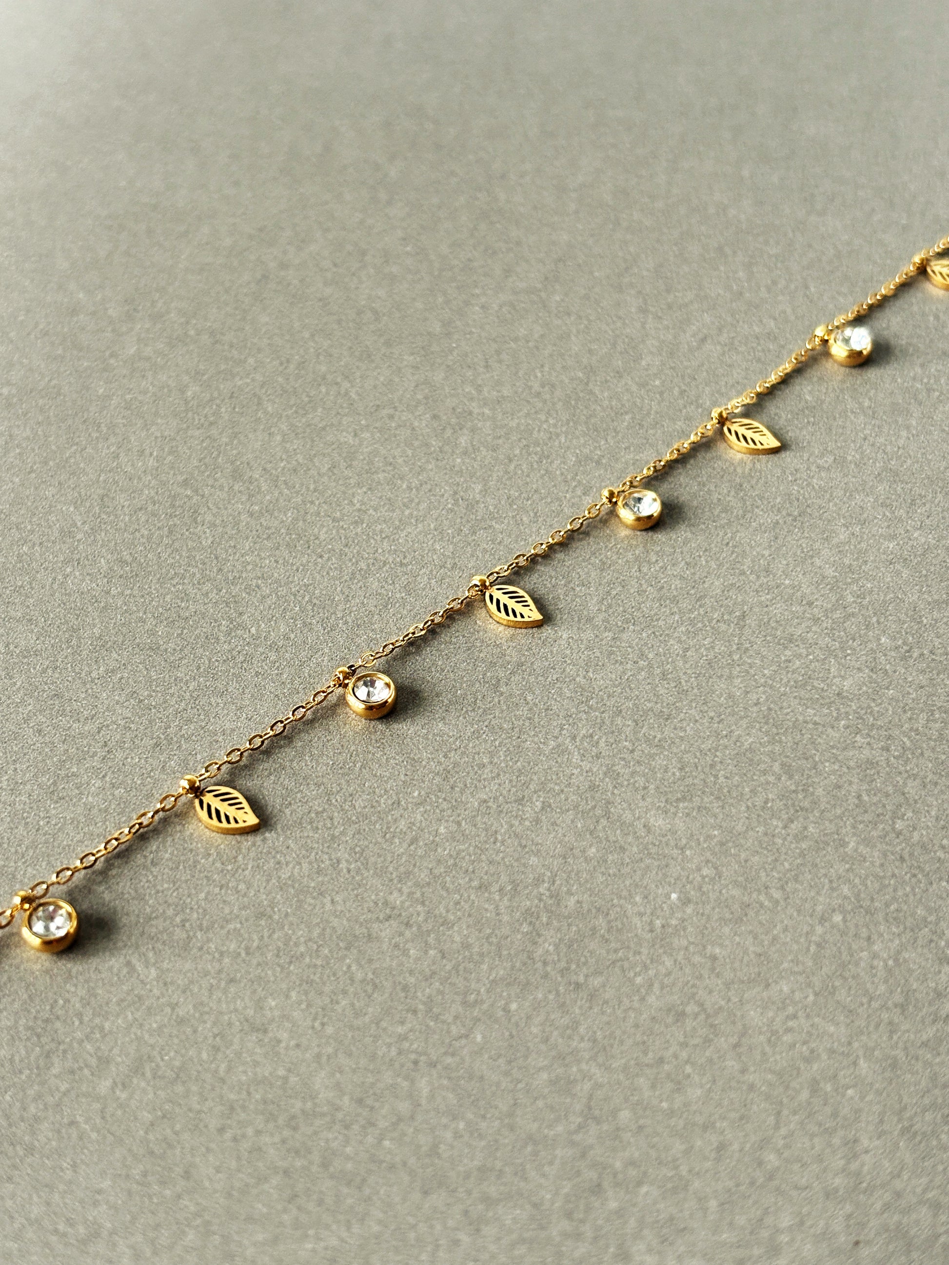 Gold bracelet with leaf and gemstone details on a gray background
