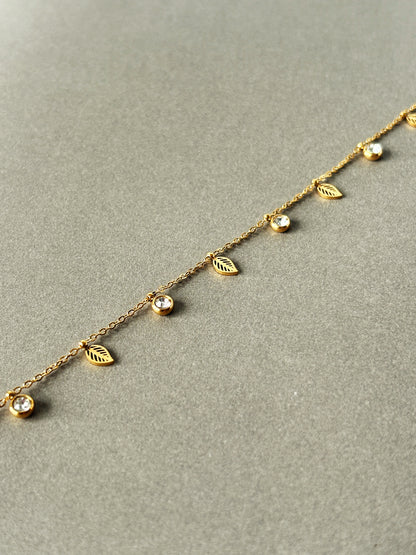 Gold bracelet with leaf and gemstone details on a gray background
