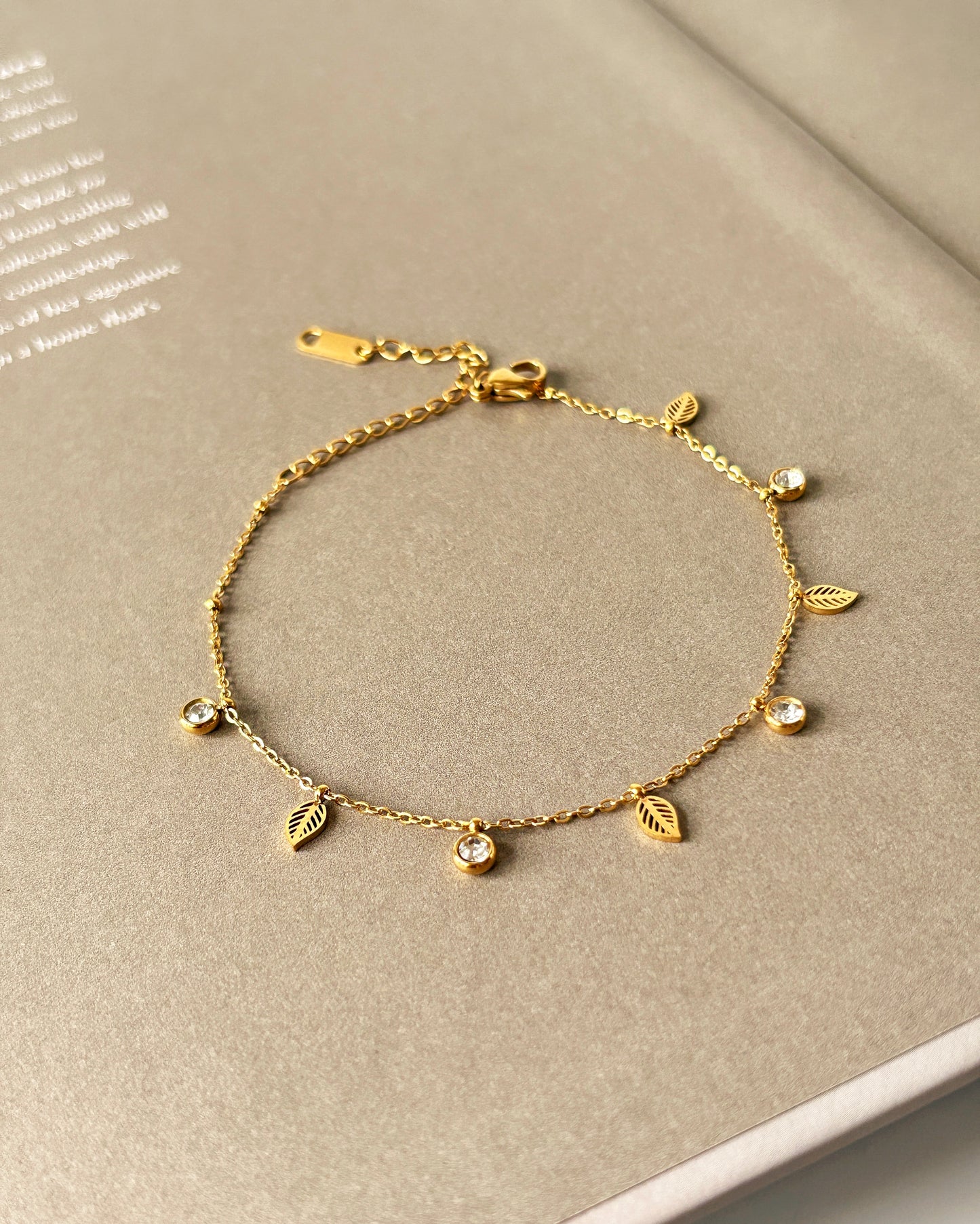 Gold bracelet with leaf-shaped charms on a beige surface