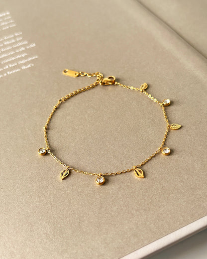 Gold bracelet with leaf-shaped charms on a beige surface