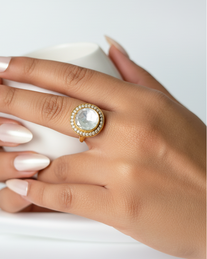 Hand wearing a gold ring with a large gemstone on a white background