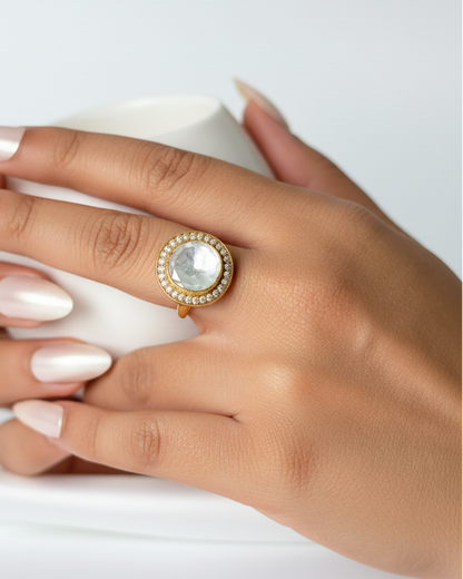 Hand wearing a gold ring with a large gemstone on a white background