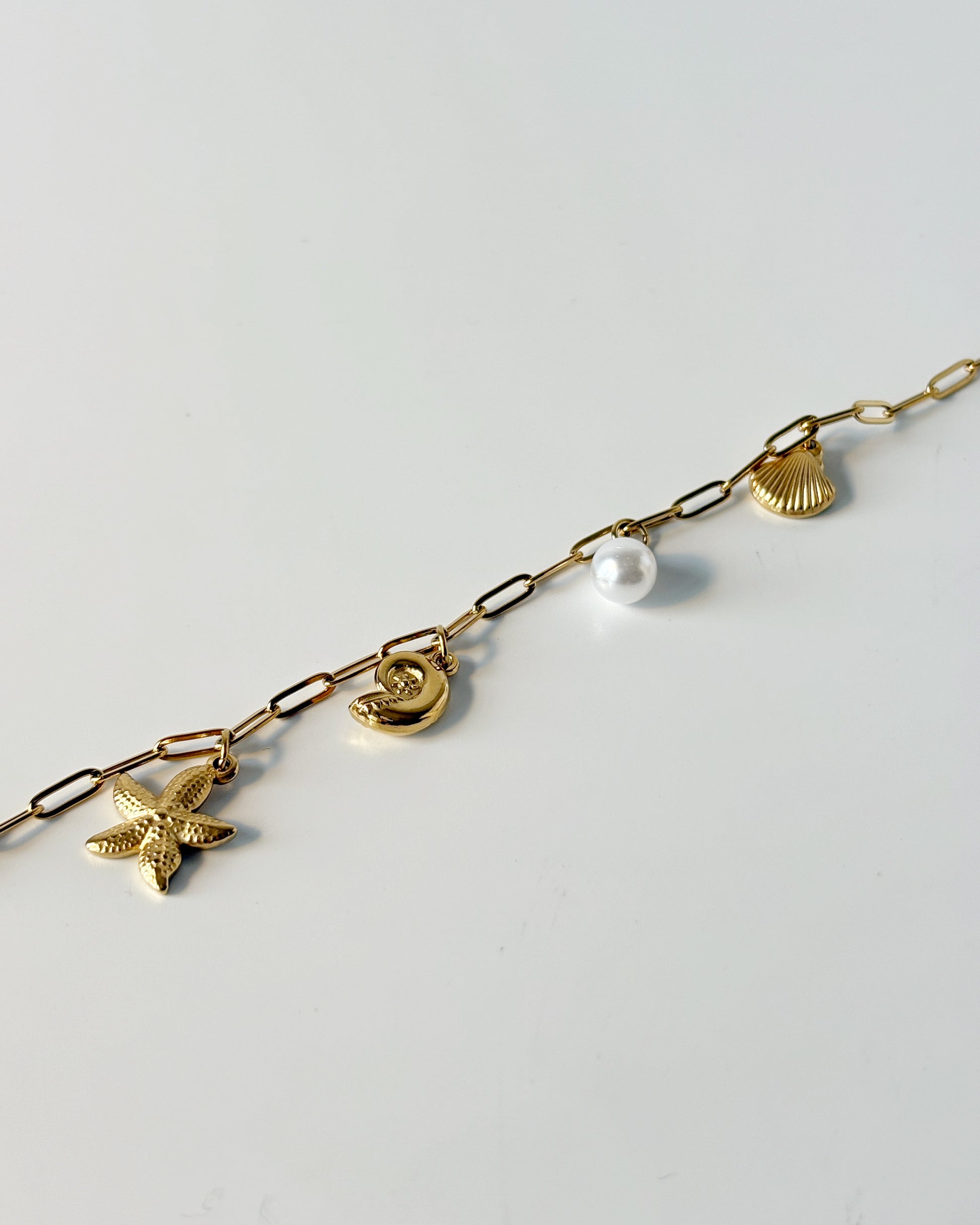 Gold chain bracelet with various charms on a light gray background