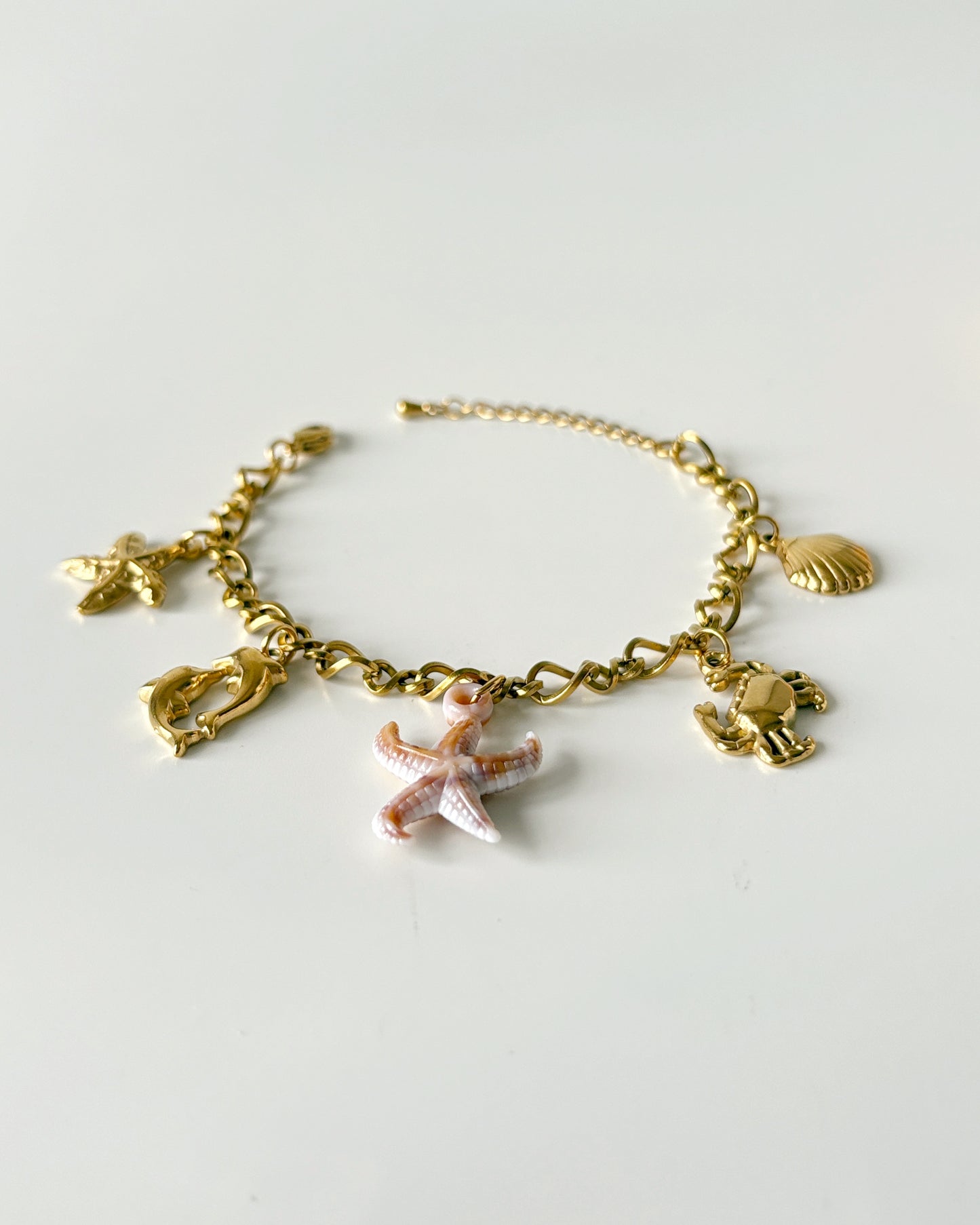 Gold bracelet with starfish and shell charms on a light gray background