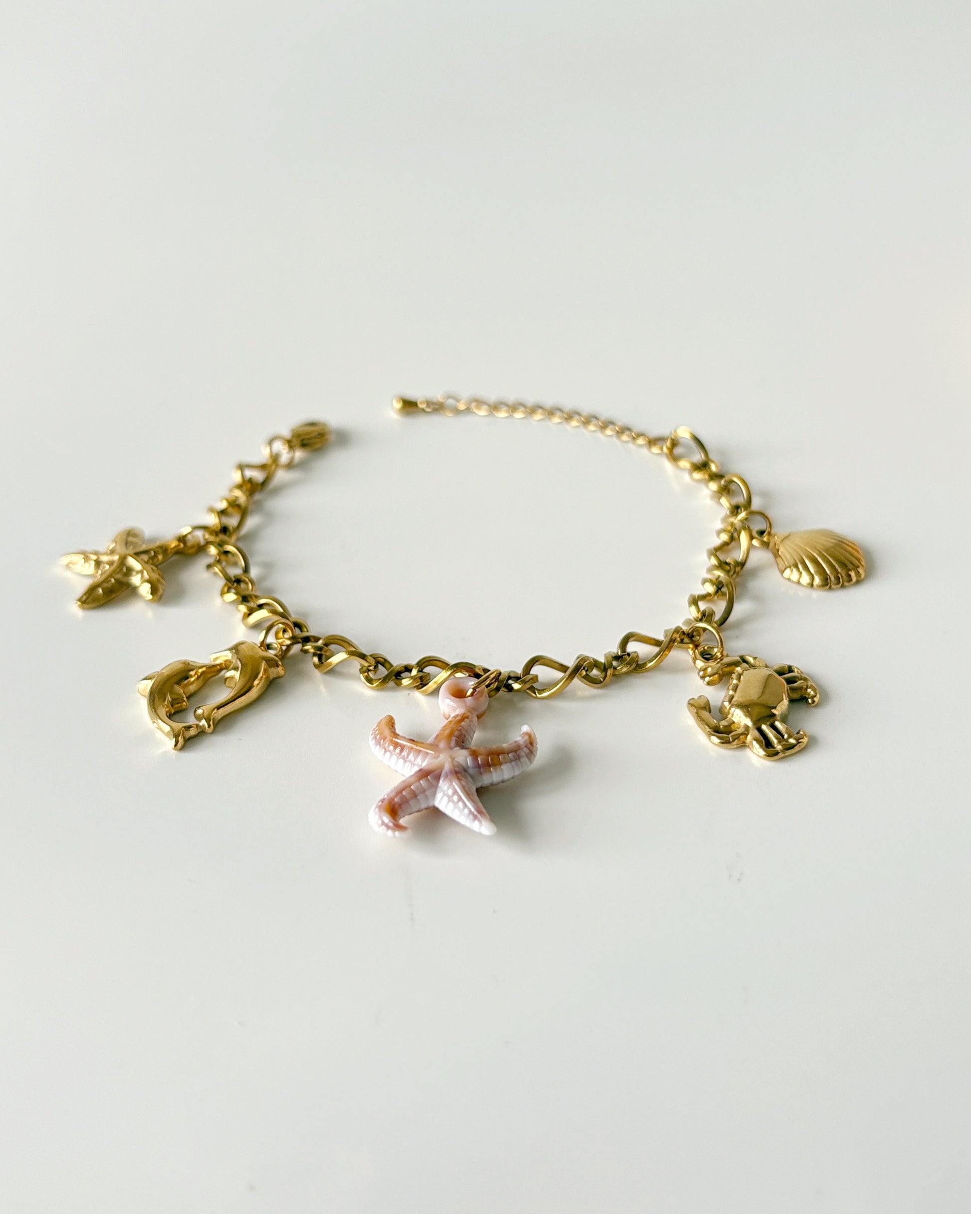 Gold bracelet with starfish and shell charms on a light gray background