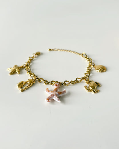 Gold bracelet with starfish and shell charms on a light gray background