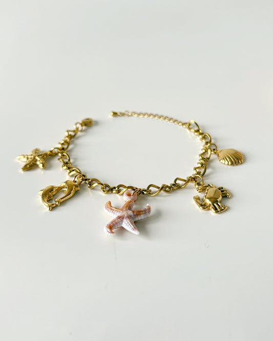 Gold bracelet with starfish and shell charms on a light gray background