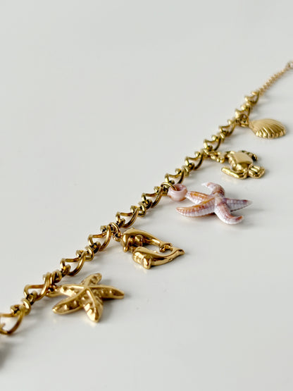 Gold necklace with various charms on a light gray background