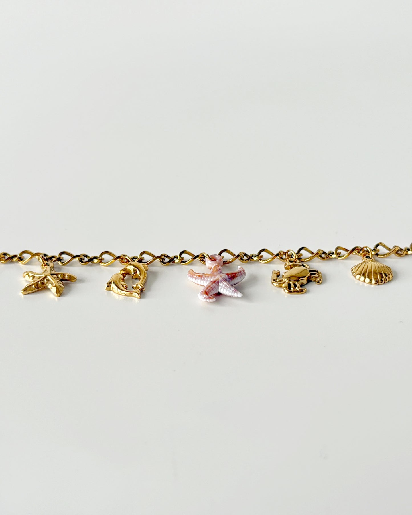Gold bracelet with various charms on a light gray background
