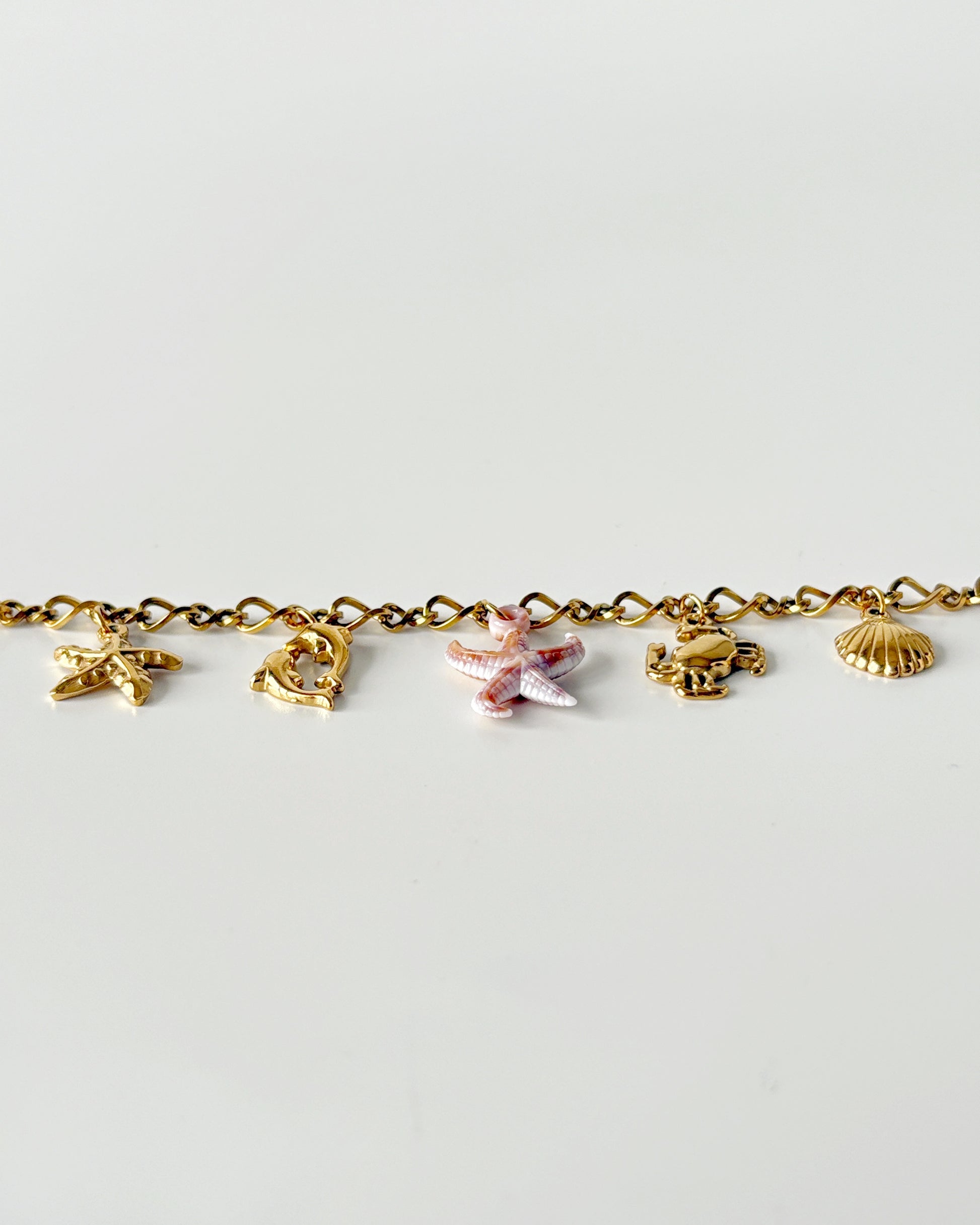 Gold bracelet with various charms on a light gray background