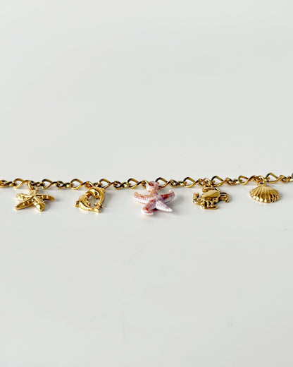 Gold bracelet with various charms on a light gray background
