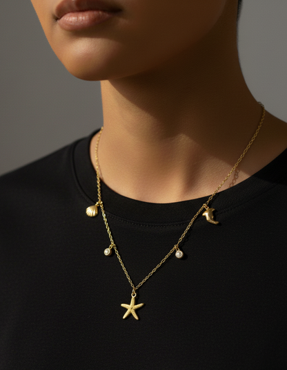 Person wearing a gold necklace with star and moon pendants on a black shirt.