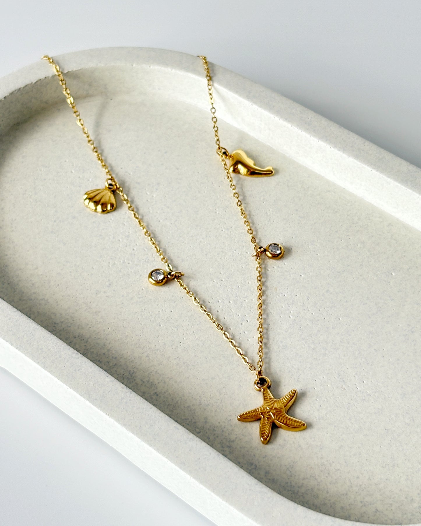 Gold necklace with starfish and shell pendants on a white dish
