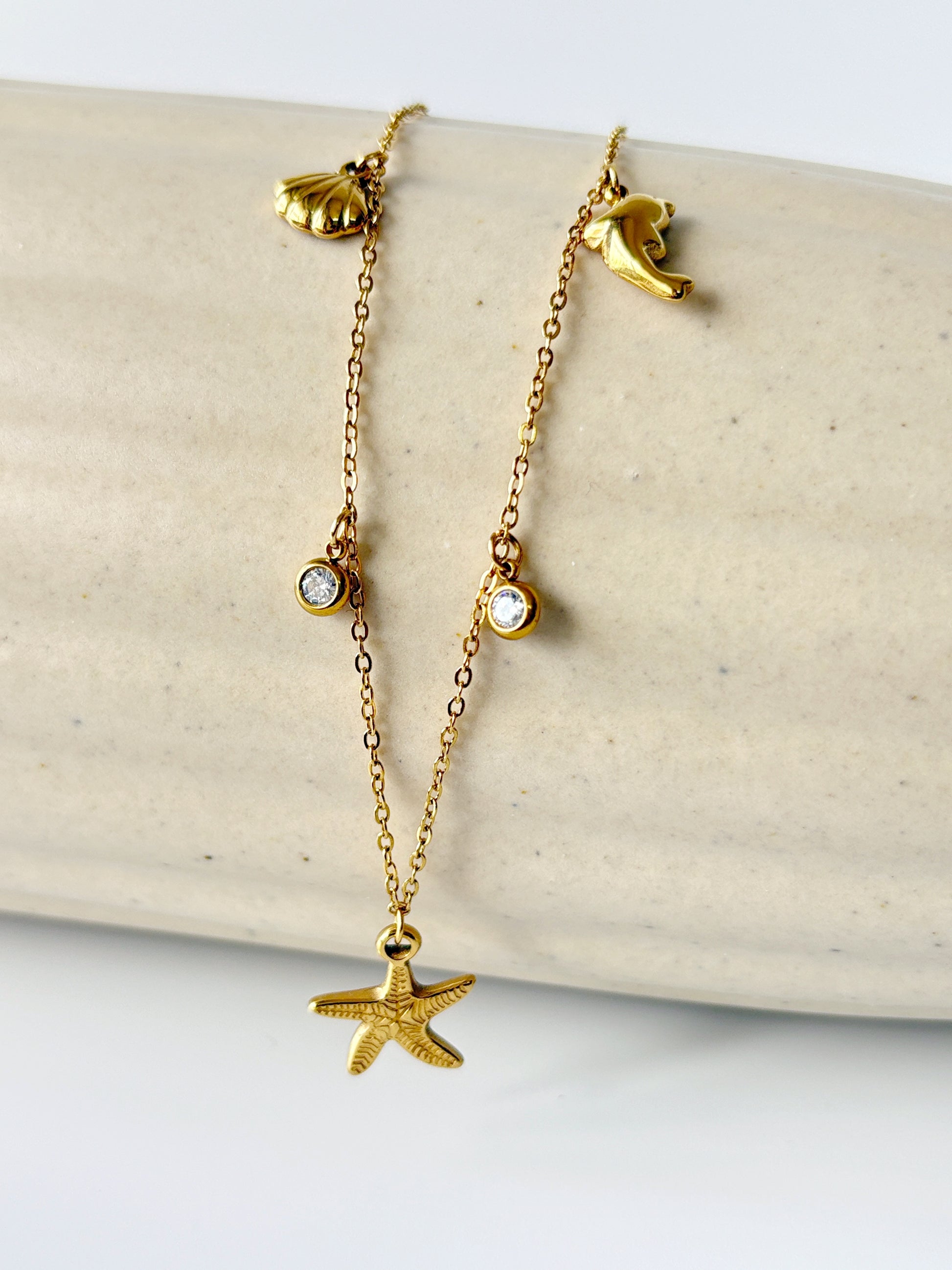 Gold necklace with starfish and shell pendants on a beige surface