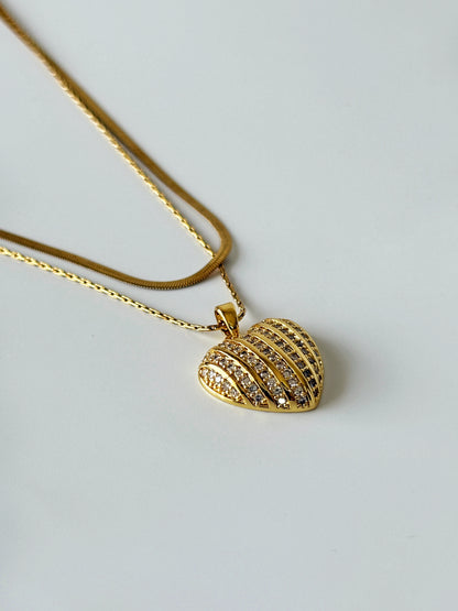 Gold necklace with a heart-shaped pendant on a light gray background