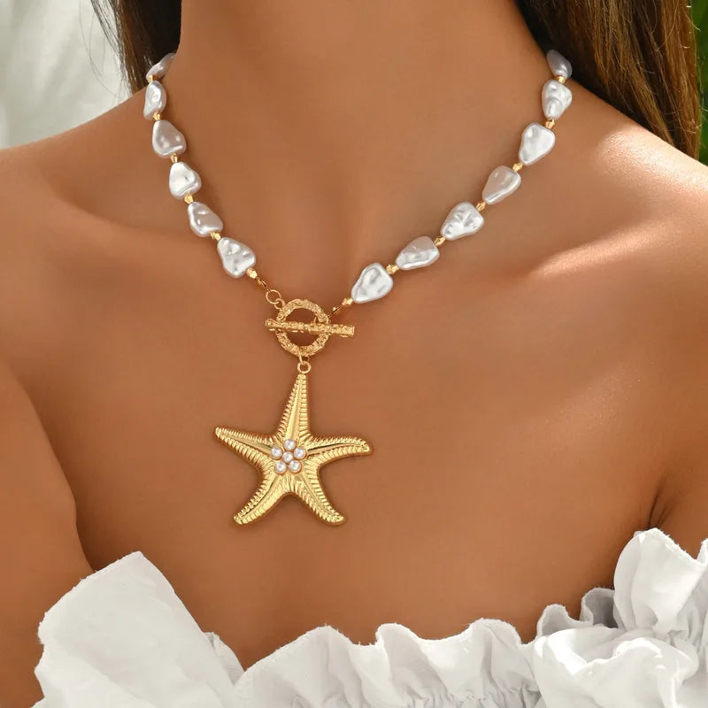 Gold starfish pendant necklace on a person wearing a white top