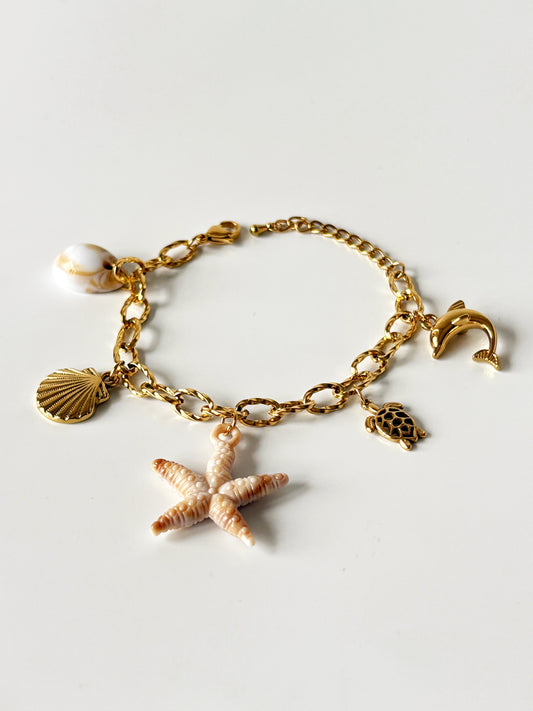Gold charm bracelet with starfish, shell, and turtle charms on a light gray background