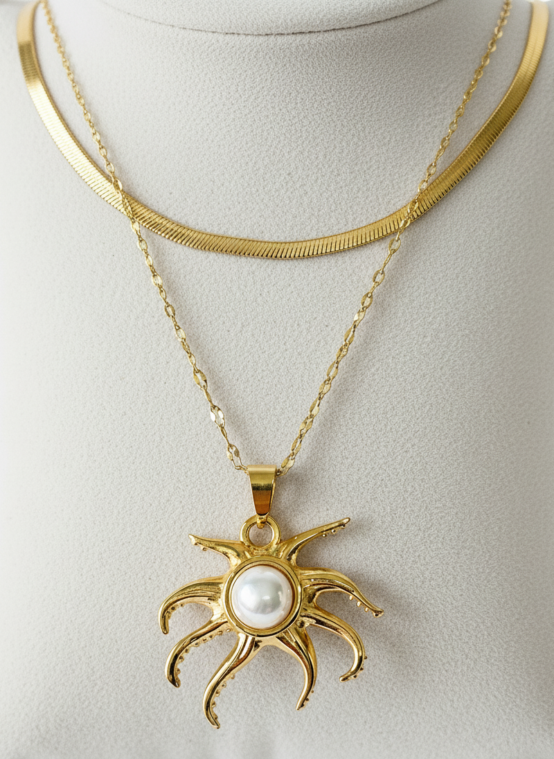 Gold necklace with a sun-shaped pendant featuring a pearl on a light gray background