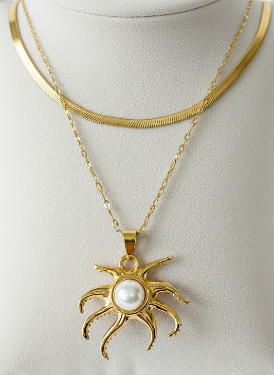 Gold necklace with a sun-shaped pendant featuring a pearl on a light gray background