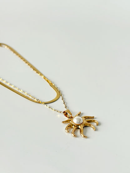 Gold spider-shaped pendant necklace with a pearl on a light gray background