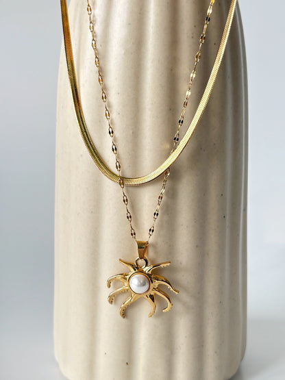 Gold necklace with a sun-shaped pendant on a beige ceramic vase.