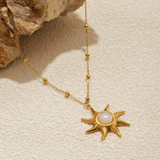 Gold necklace with a sun-shaped pendant on a textured beige surface