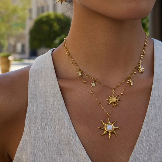 Gold necklace with sun and moon pendants worn by a person outdoors.